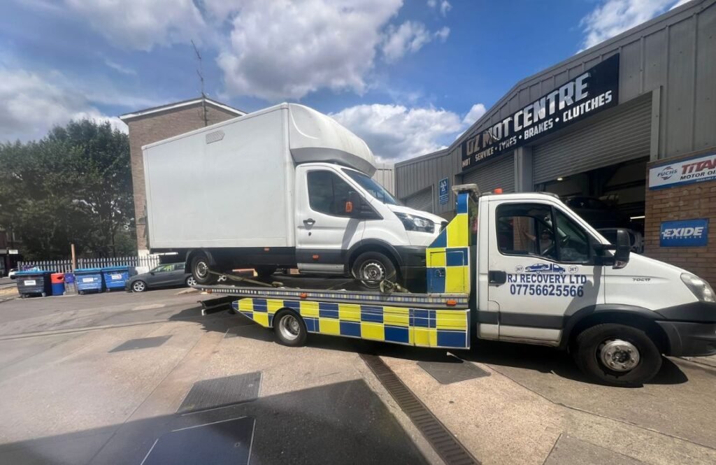 RJ Recovery London transporting a white delivery van securely on a flatbed outside a London centre