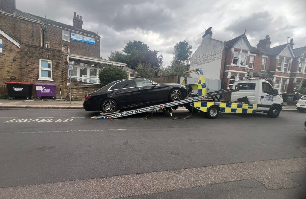 RJ Recovery London towing a black car at an angle on a residential London street